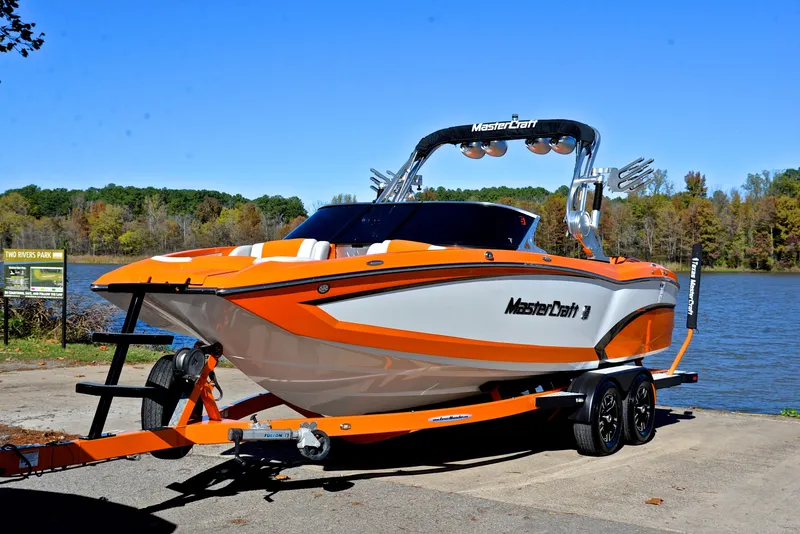 Slide: The Image of 2015 MasterCraft X23 boat in orange and white, parked by a lake. - 10