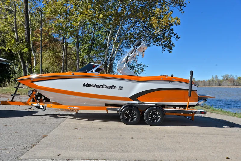 Slide: The Image of 2015 MasterCraft X23 boat on trailer by a lake, featuring orange and white design. - 11