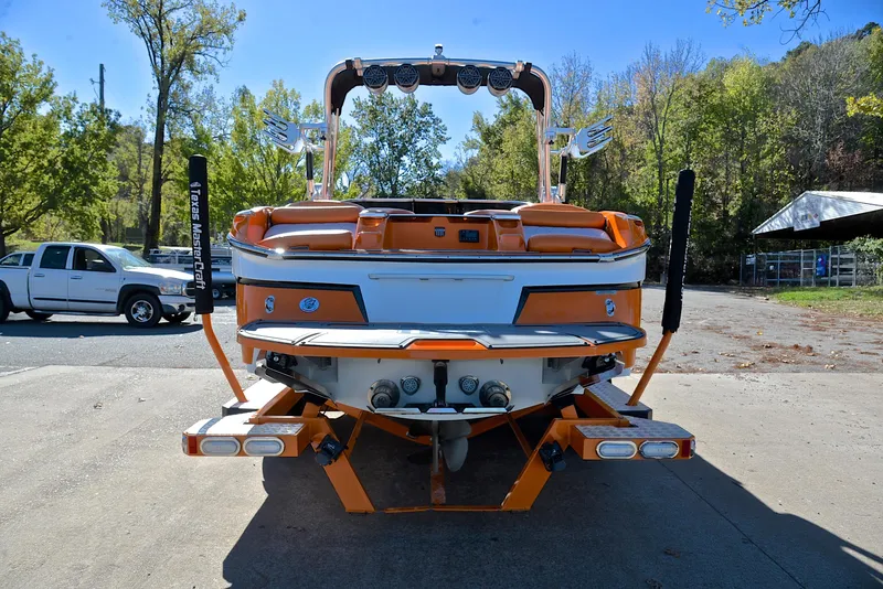 Slide: The Image of 2015 MasterCraft X23 boat, orange and white, parked outdoors with trees in the background. - 13