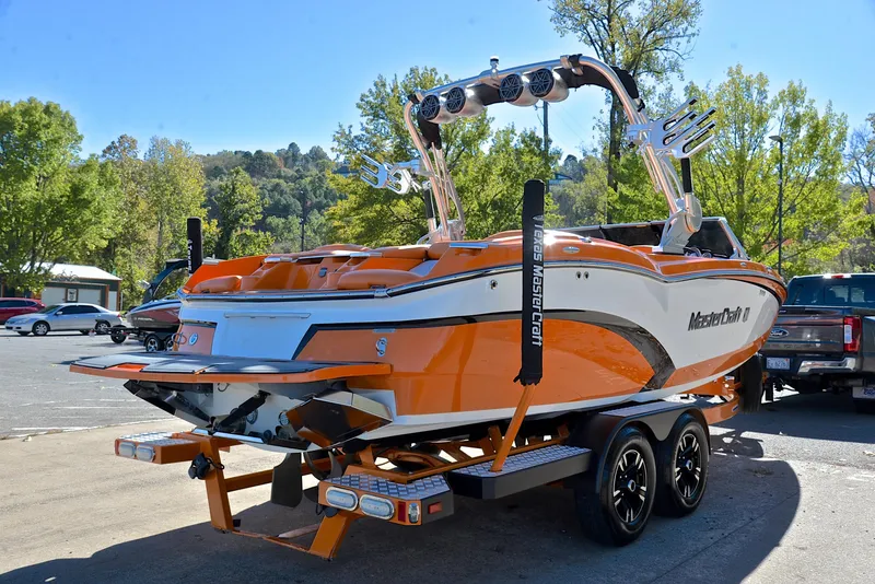 Slide: The Image of 2015 MasterCraft X23 boat in orange and white on a trailer, parked outdoors. - 14