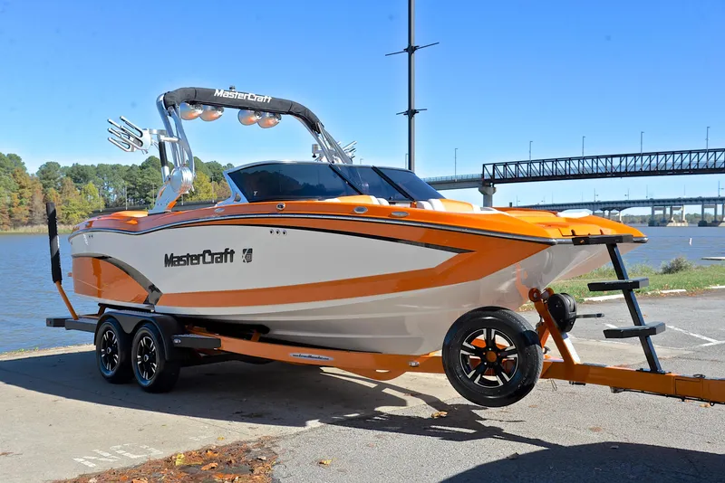 Slide: The Image of 2015 MasterCraft X23 boat in orange and white, parked near a river with a bridge. - 16