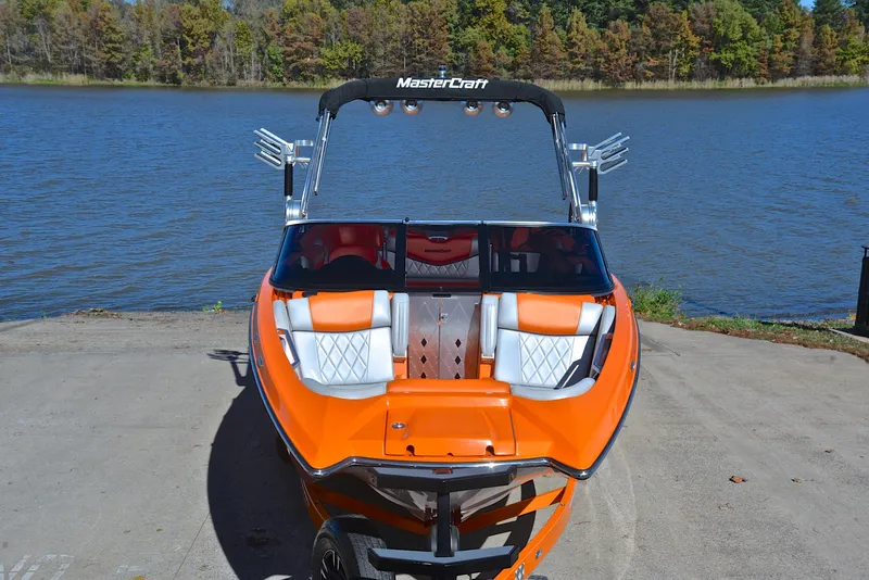 Slide: The Image of 2015 MasterCraft X23 boat, orange exterior, docked by a serene lake. - 17