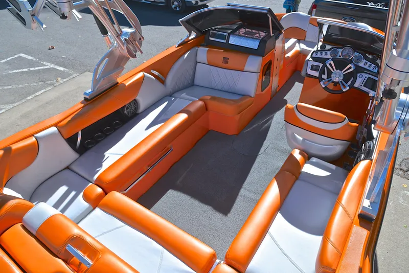 Slide: The Image of 2015 MasterCraft X23 boat interior with orange and white seating, modern dashboard, and spacious layout. - 19
