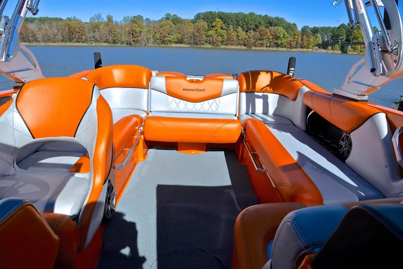 Slide: The Image of 2015 MasterCraft X23 boat interior with orange and white seating on a lake. - 22