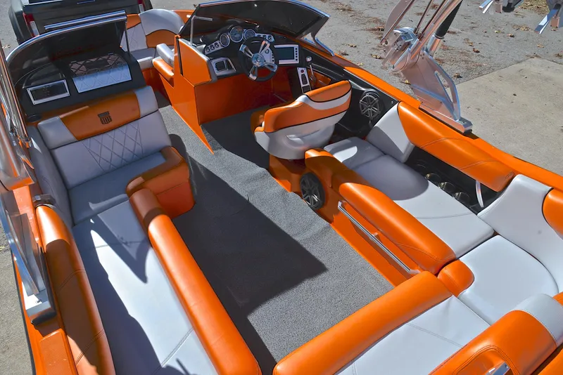 Slide: The Image of 2015 MasterCraft X23 boat interior with orange and white seating, modern dashboard, and spacious layout. - 23