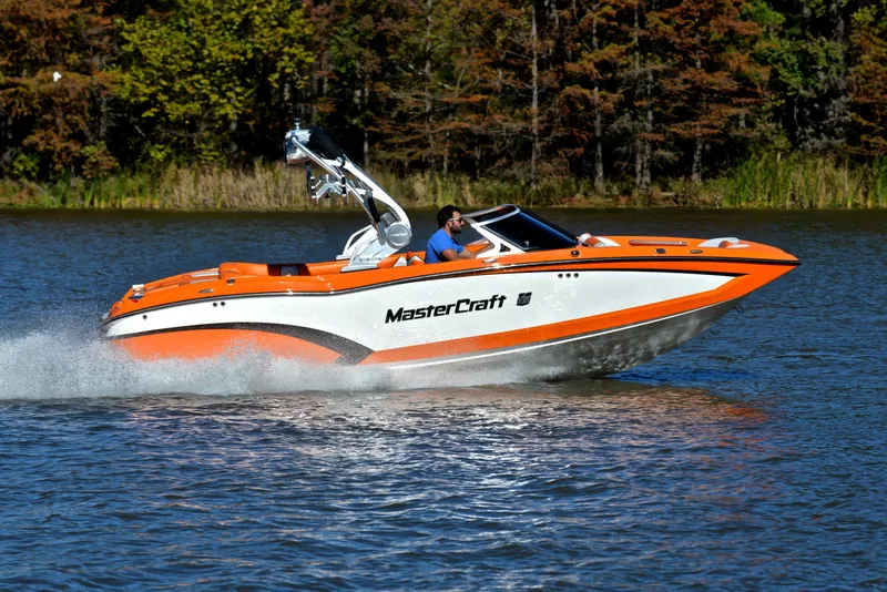 Slide: The Image of 2015 MasterCraft X23 boat cruising on a lake with vibrant orange and white design. - 3