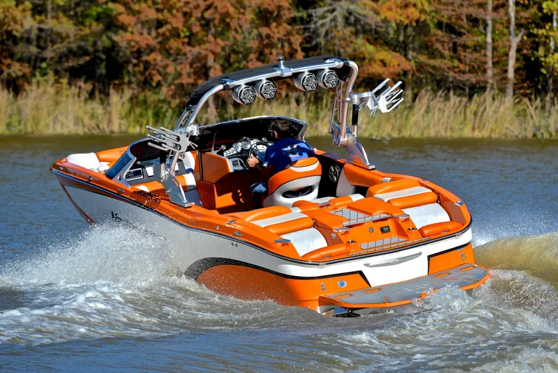 Slide: The Image of 2015 MasterCraft X23 boat cruising on a lake with vibrant orange and white design. - 6