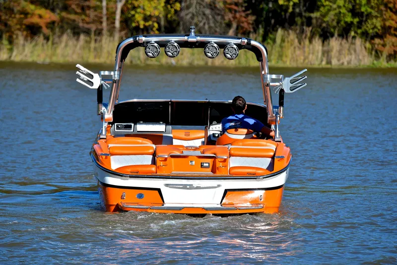 Slide: The Image of 2015 MasterCraft X23 boat on water, orange exterior, rear view, surrounded by trees. - 8