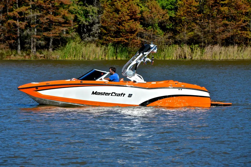 Slide: The Image of 2015 MasterCraft X23 boat cruising on a lake with lush green trees in the background. - 9