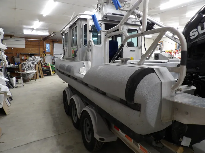 Slide: The Image of 2005 SAFE Boats Defender 25 in a garage, showcasing its robust design and triple-axle trailer. - 16