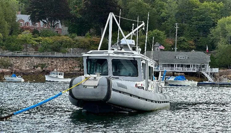 Slide: The Image of SAFE Boats Defender 25, 2005 model, moored in a scenic harbor with surrounding boats. - 2
