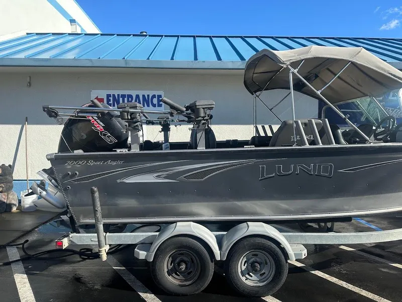 Slide: The Image of 2019 Lund 2000 Sport Angler boat on trailer, parked near building with blue roof. - 13
