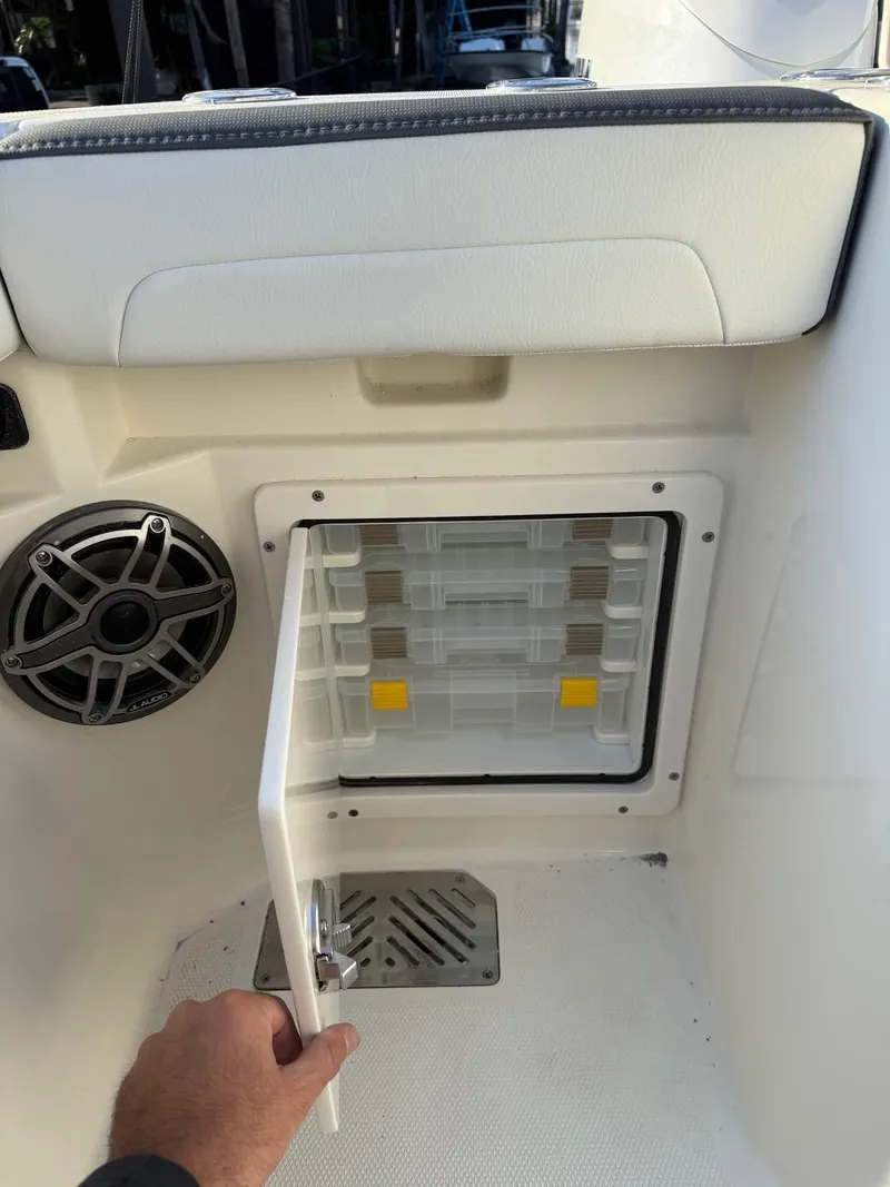 Slide: The Image of 2025 Cobia 265 Open Center Console storage compartment with speaker and hand opening door. - 17
