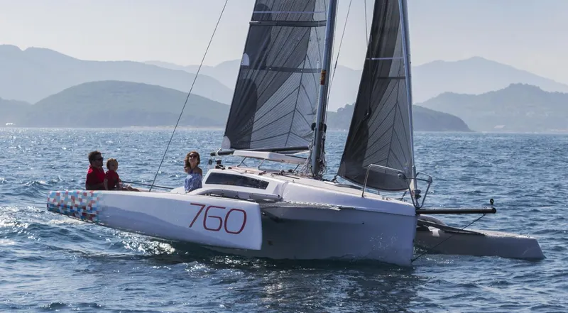 Slide: The Image of Sailing on a 2025 Corsair 760 trimaran in open waters, with scenic mountain backdrop. - 1