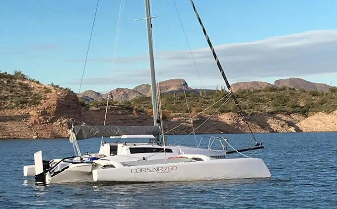 The Image of Sleek Corsair 760 trimaran sailing on a serene lake, surrounded by rocky hills, 2025 model. - 0