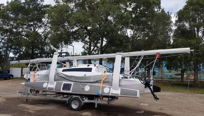 Slide: The Image of Corsair 760 trimaran sailboat on trailer, 2025 model, parked outdoors with trees in background. - 11
