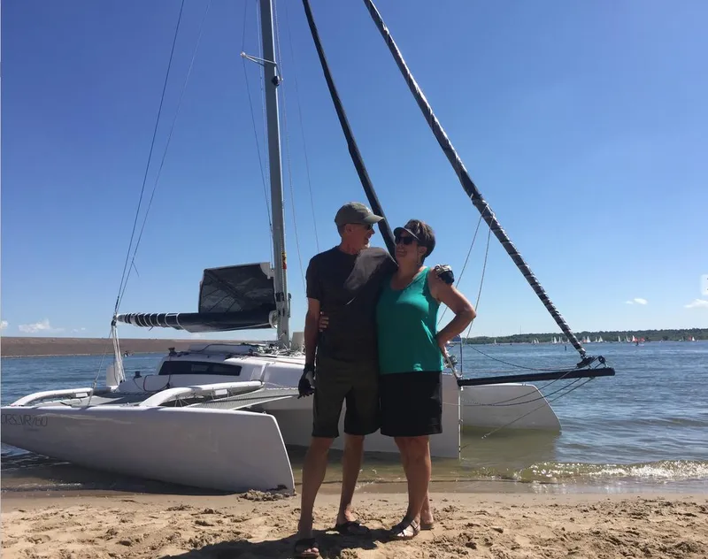 Slide: The Image of Couple standing on beach with Corsair 760 sailboat in background, sunny day, 2025 model. - 2