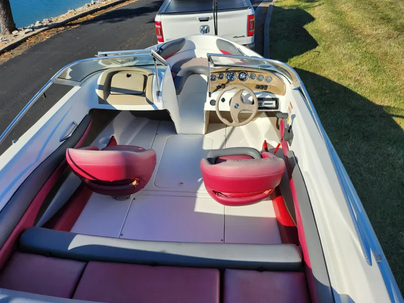 Slide: The Image of 2003 Larson SEi 180 boat interior with red seats and dashboard, parked near a truck. - 10
