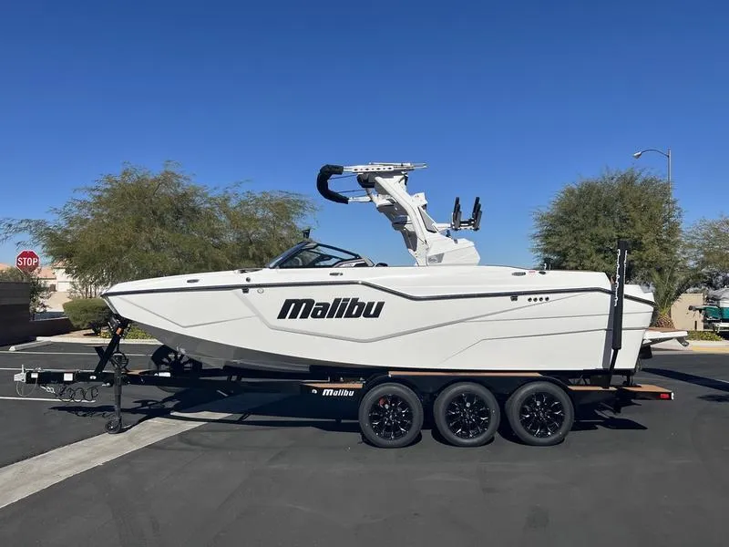 Slide: The Image of 2025 Malibu M230 boat on trailer, parked outdoors under clear blue sky. - 1