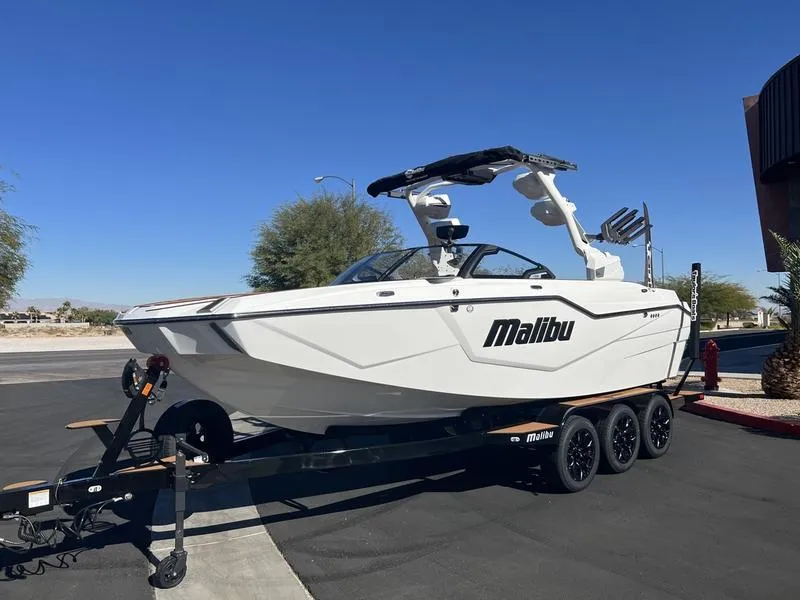 Slide: The Image of 2025 Malibu M230 boat on trailer, parked outdoors under clear blue sky. - 2