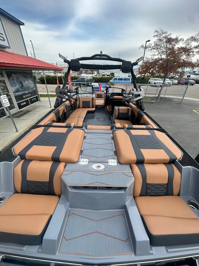 Slide: The Image of 2025 Malibu 24 MXZ boat interior with tan and black seating, docked at a marina. - 10