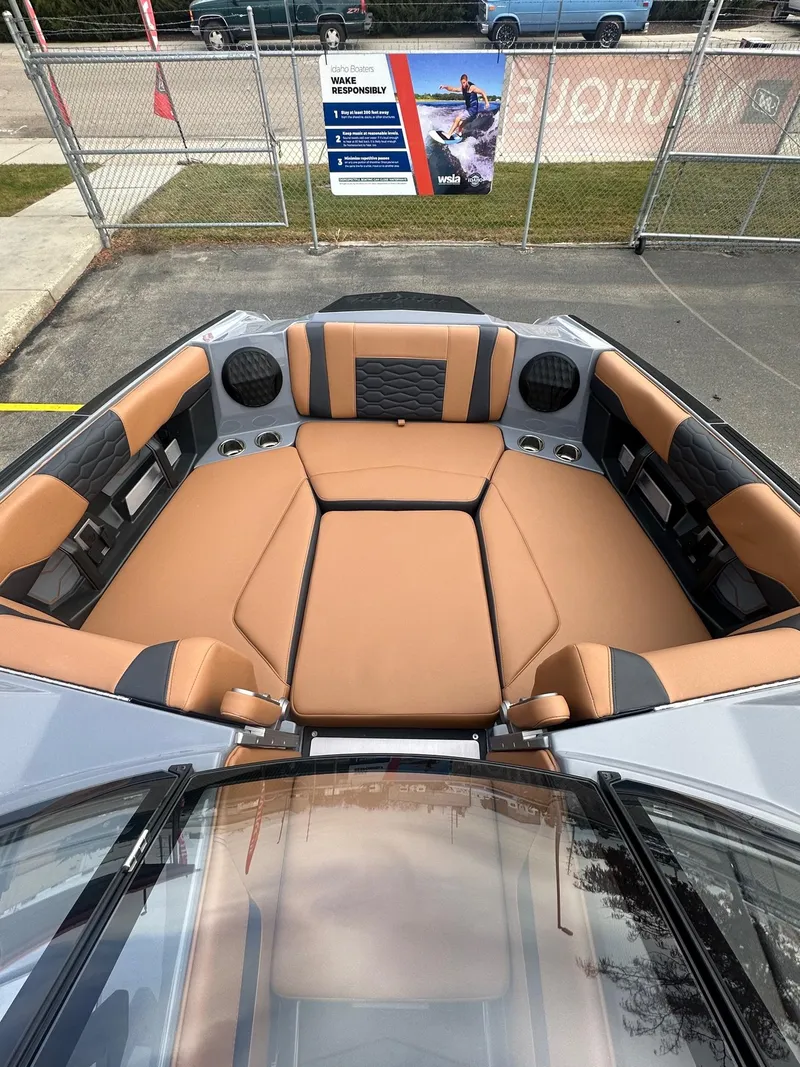 Slide: The Image of 2025 Malibu 24 MXZ boat interior with tan and black seating, outdoor display setting. - 13