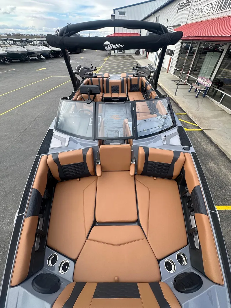 Slide: The Image of 2025 Malibu 24 MXZ boat with luxurious tan and black seating, docked at a marina. - 14
