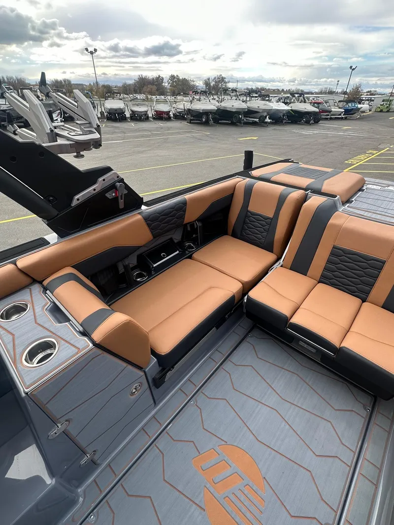 Slide: The Image of 2025 Malibu 24 MXZ boat interior with tan and black seating, docked in a marina. - 15