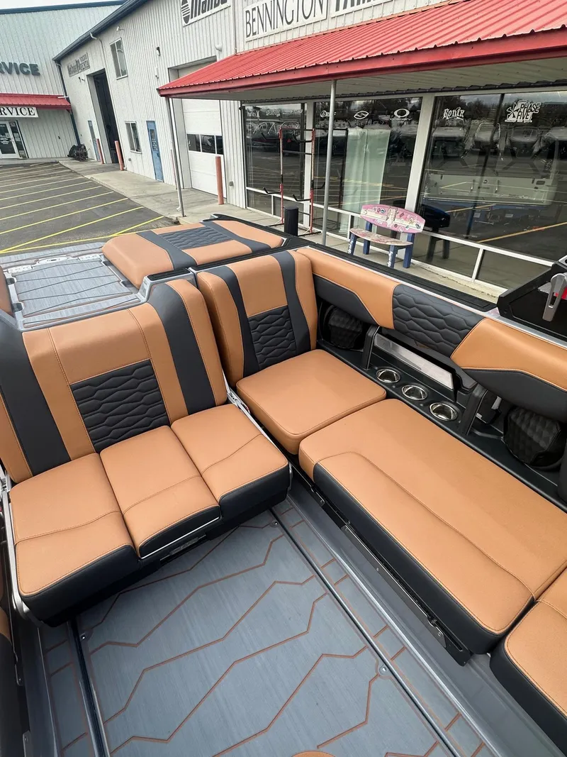 Slide: The Image of 2025 Malibu 24 MXZ boat interior with tan and black seating, parked outside dealership. - 16