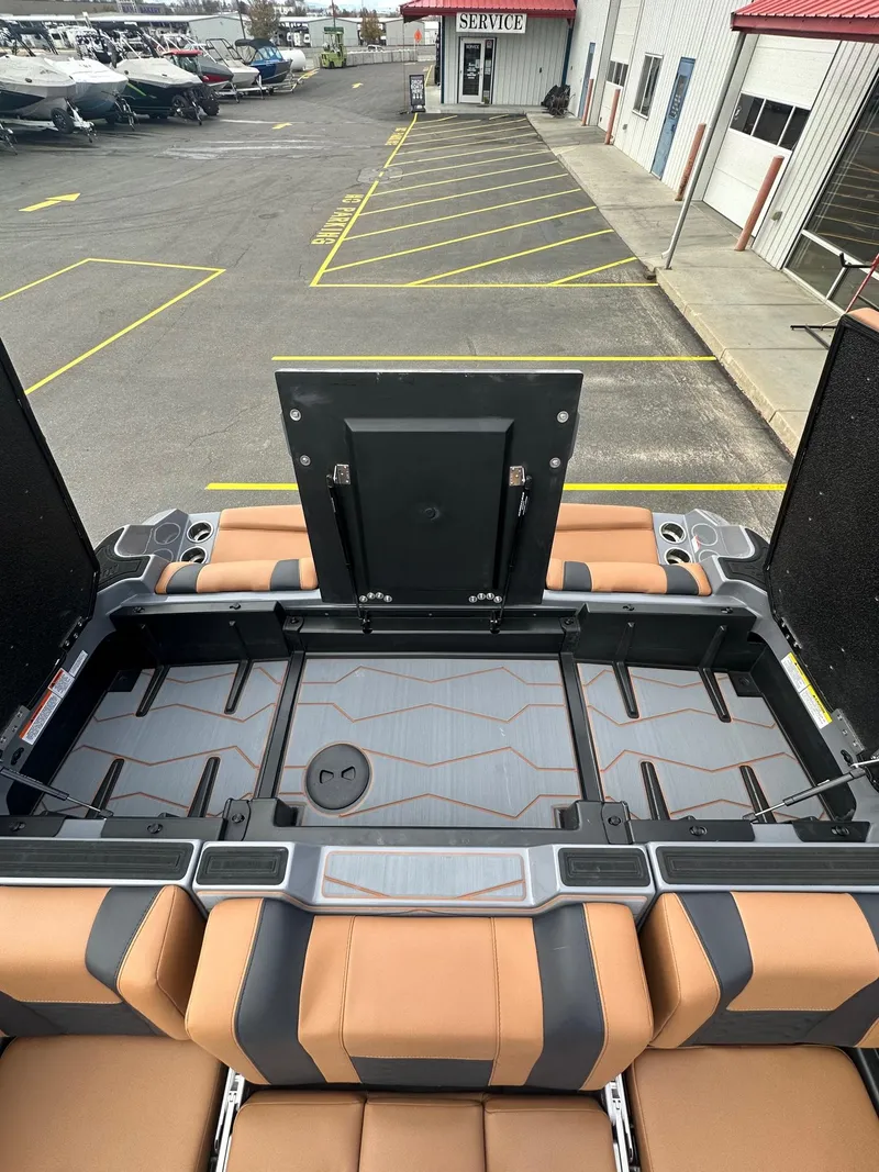 Slide: The Image of 2025 Malibu 24 MXZ boat interior with tan and black seating, open storage compartment. - 20