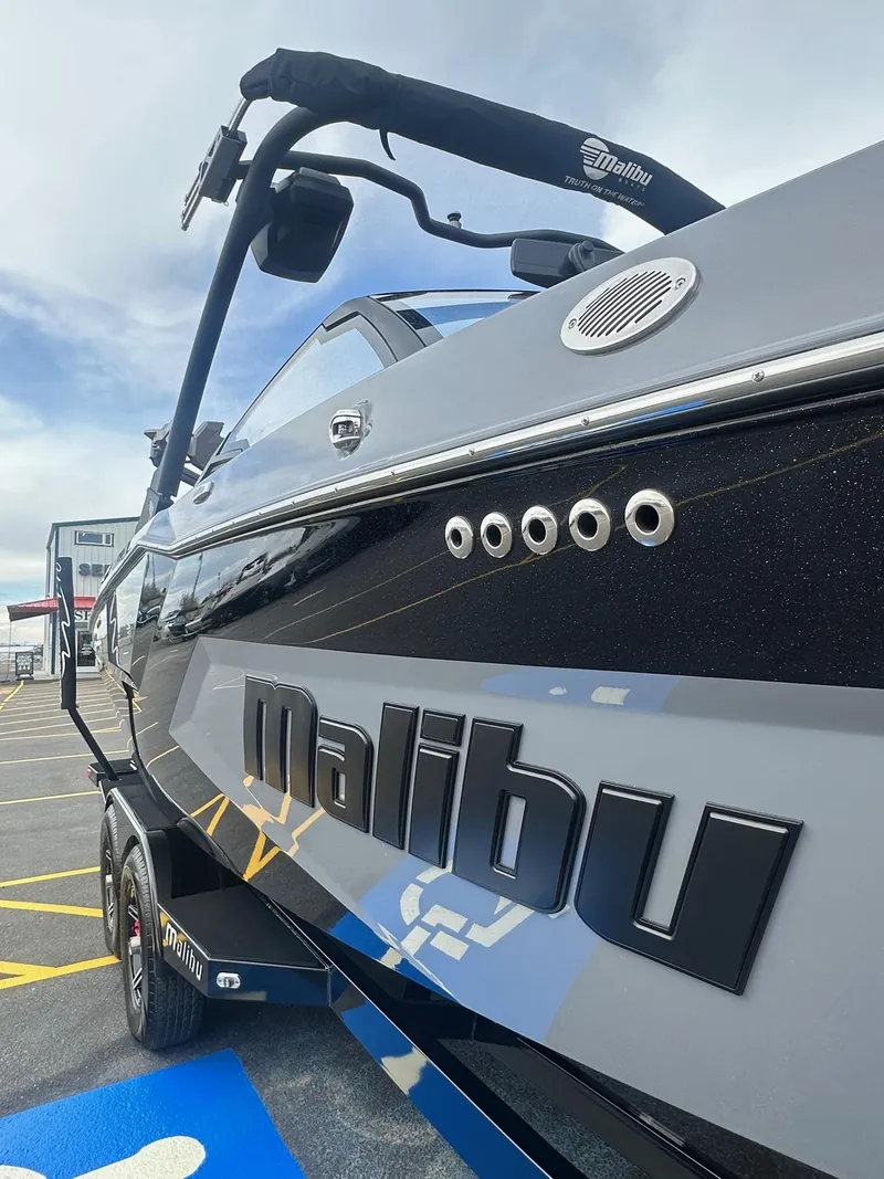 Slide: The Image of 2025 Malibu 24 MXZ boat, sleek black design, parked outdoors on a sunny day. - 3