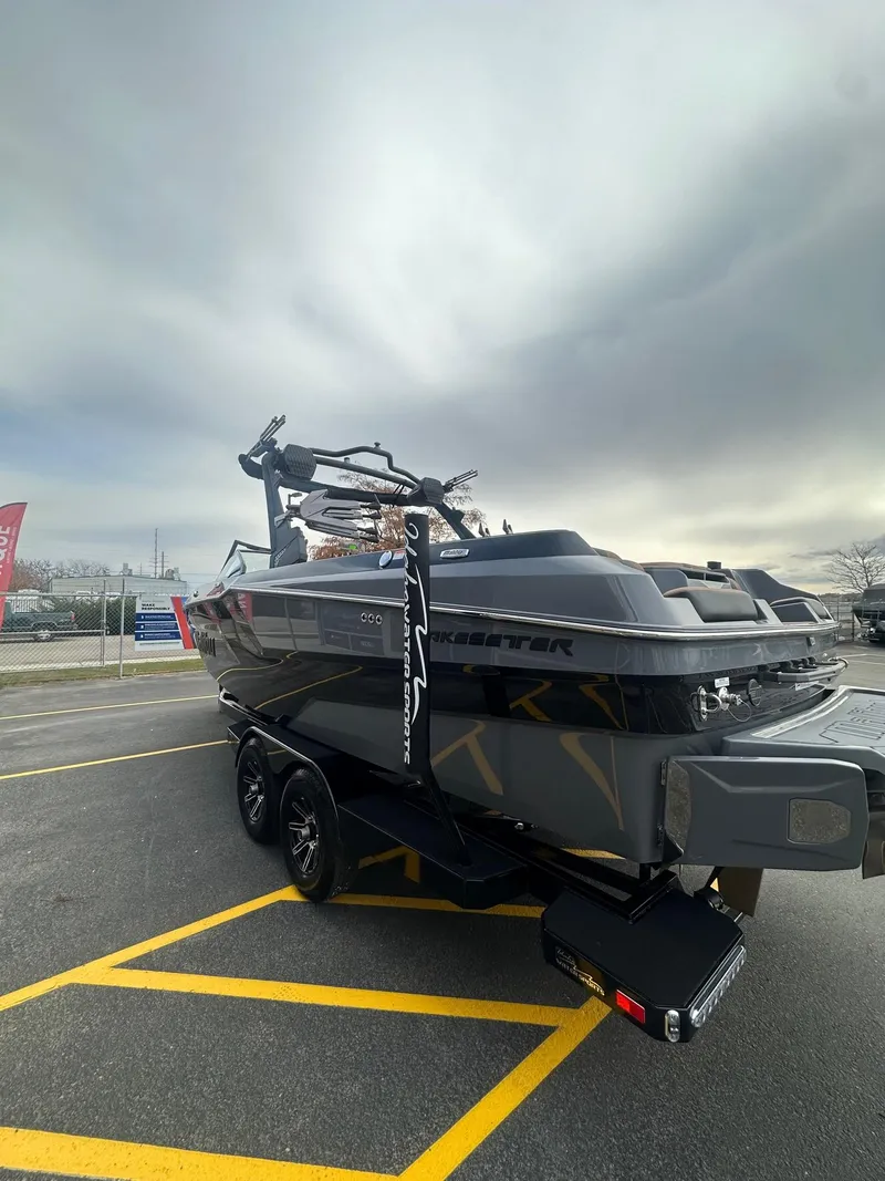 Slide: The Image of 2025 Malibu 24 MXZ boat on trailer, parked in a lot under cloudy sky. - 8
