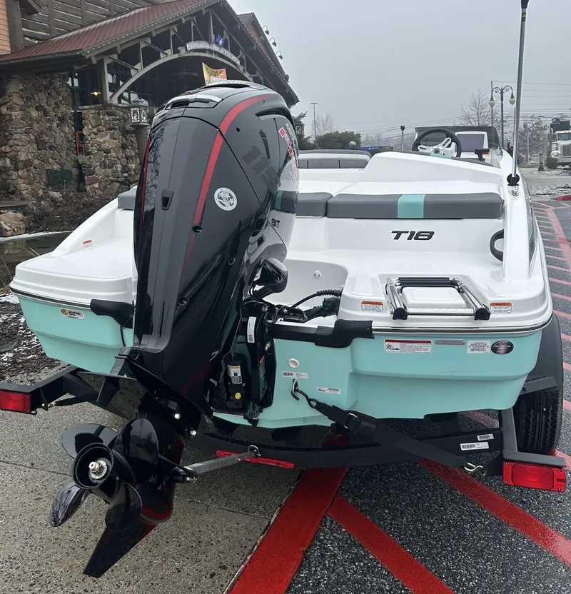 Slide: The Image of 2025 Tahoe T18 boat with outboard motor on trailer, parked near rustic building. - 2