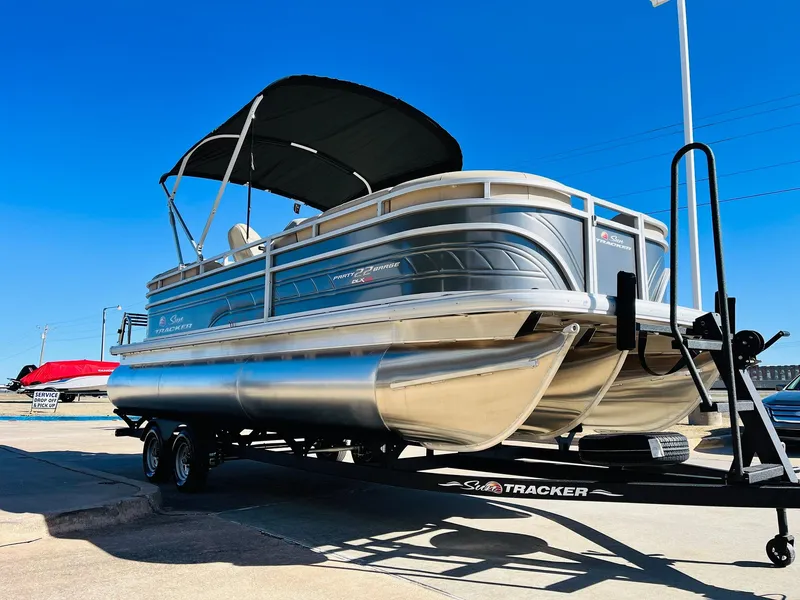 Slide: The Image of 2025 Sun Tracker Party Barge 22 RF XP3 pontoon boat on trailer, under clear blue sky. - 3