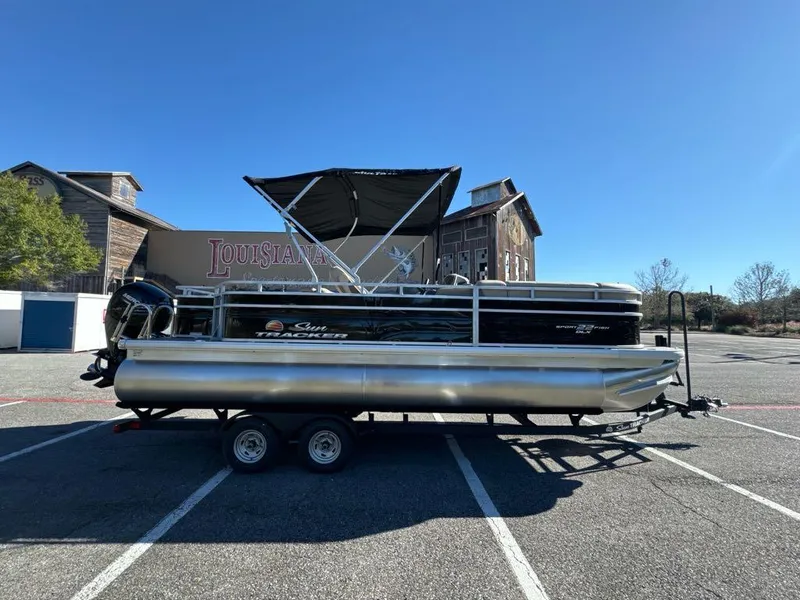 Slide: The Image of 2025 Sun Tracker SportFish 22 DLX pontoon boat parked in a lot under clear blue sky. - 2