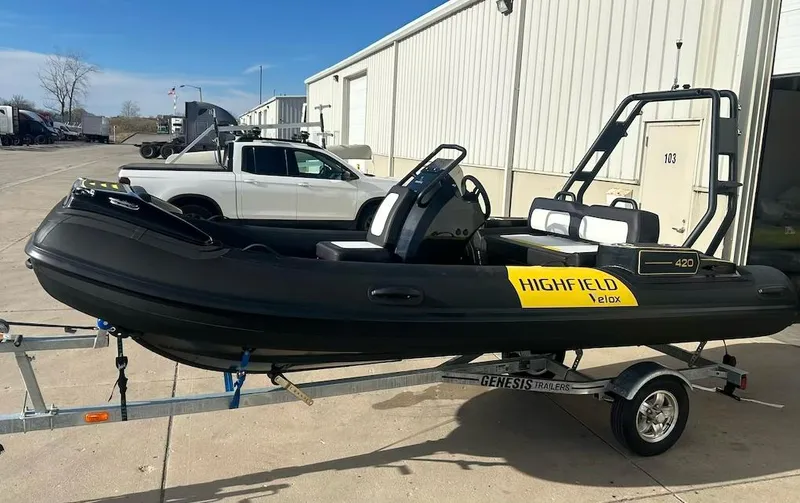 Slide: The Image of 2025 Highfield Velox 420 inflatable boat on trailer, parked outside a warehouse. - 2