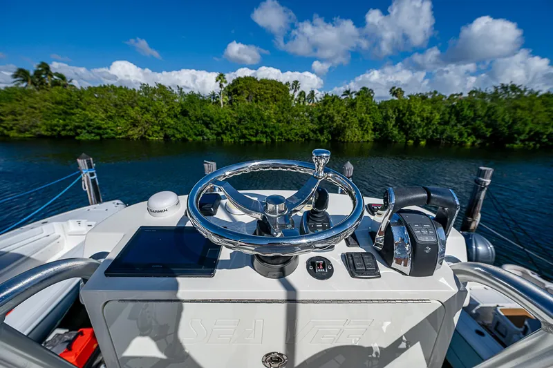 Slide: The Image of 2018 SeaVee 370z boat helm with steering wheel and controls, surrounded by lush greenery. - 53