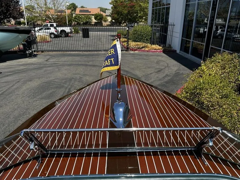 Slide: The Image of 1994 Hacker-Craft 26' Runabout with polished wood finish and flag, parked outdoors. - 6