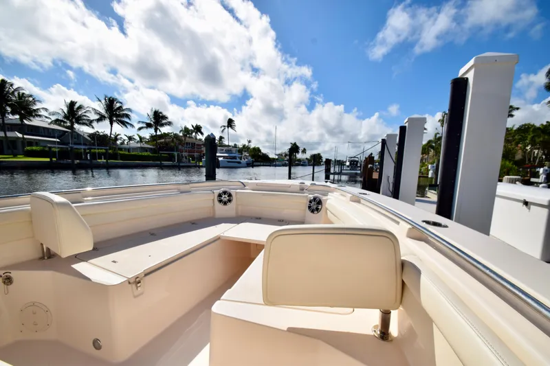 Slide: The Image of 2023 Grady-White 336 Canyon boat interior with seating, docked by palm trees under blue sky. - 84