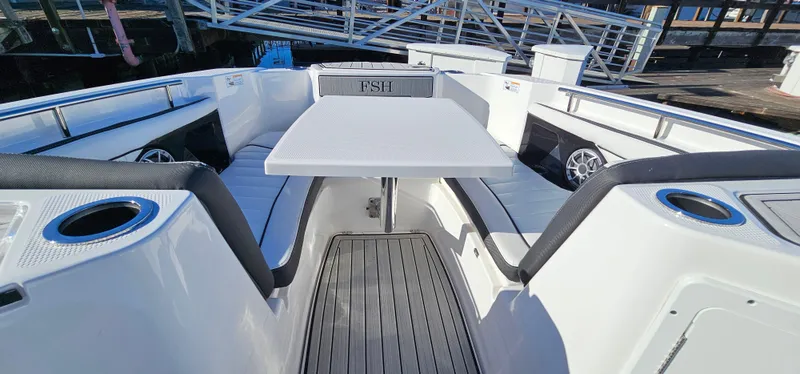 Slide: The Image of 2023 Yamaha Boats 255 FSH Sport E interior with seating and table, docked at marina. - 17