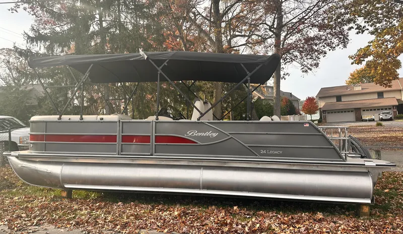 Slide: The Image of 2025 Bentley Pontoons Legacy 243 Swingback, gray with red accents, parked outdoors in autumn setting. - 6