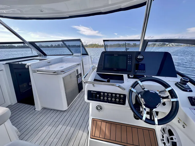 Slide: The Image of Aquila 32 Sport 2020 yacht interior with steering wheel and control panel on open water. - 14