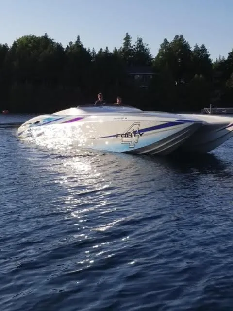 Slide: The Image of 2006 MTI 44 Pleasure Cat boat on calm water with forested background. - 2