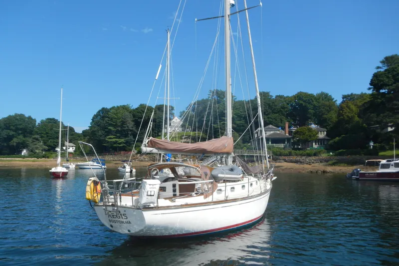 Slide: The Image of 1986 Cape Dory 36 sailboat anchored in a scenic harbor with trees and houses. - 2