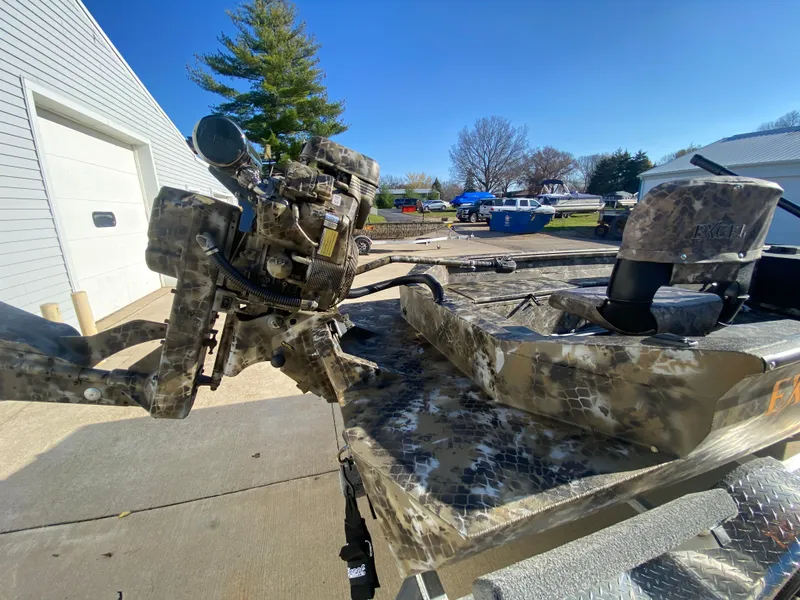 Slide: The Image of 2025 Excel 1854 F4 Shallow Water boat with camouflage design and motor, parked outdoors. - 31