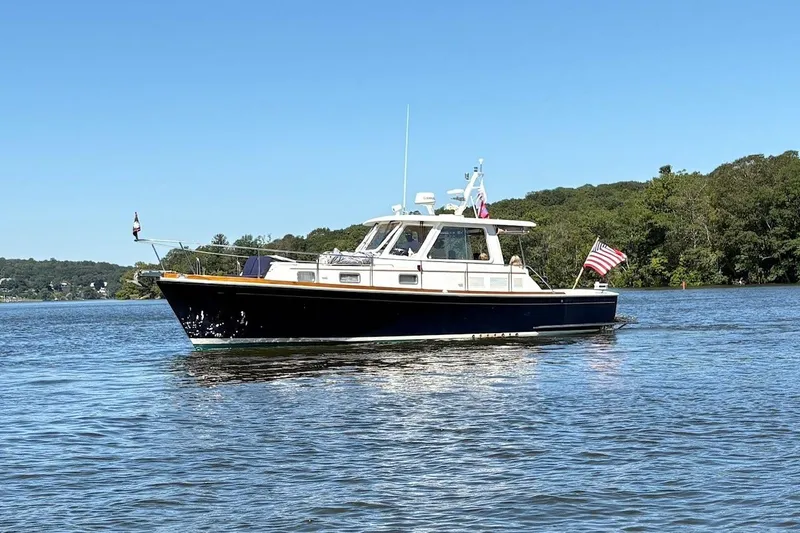 The Image of 2001 Grand Banks Eastbay 38 HX yacht cruising on a serene lake with lush green shoreline. - 0