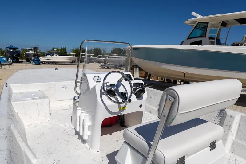 Slide: The Image of 2025 Coastal Skiff 184 boat interior with steering console and seating, docked under clear blue sky. - 14