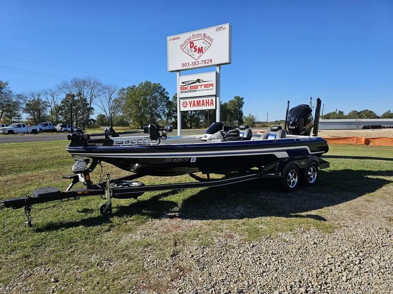 The Image of 2013 Skeeter 21i boat on trailer near dealership sign, clear blue sky. - 1