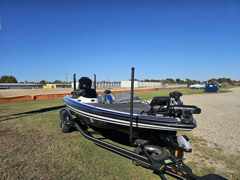 Slide: The Image of 2013 Skeeter 21i boat on trailer, parked on grassy area under clear blue sky. - 2