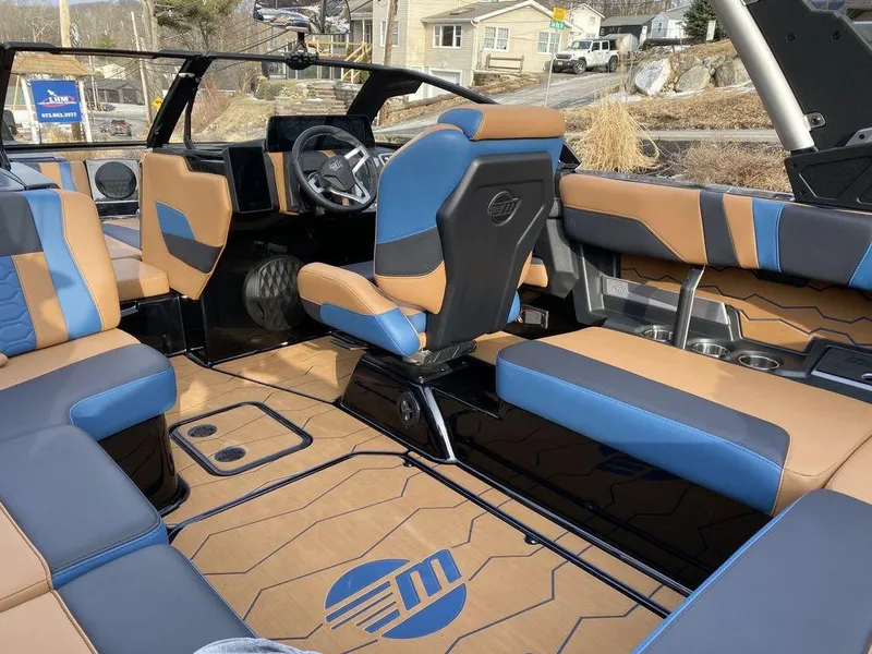 Slide: The Image of 2025 Malibu Wakesetter 22 MXZ boat interior with tan and blue seating, parked outdoors. - 11